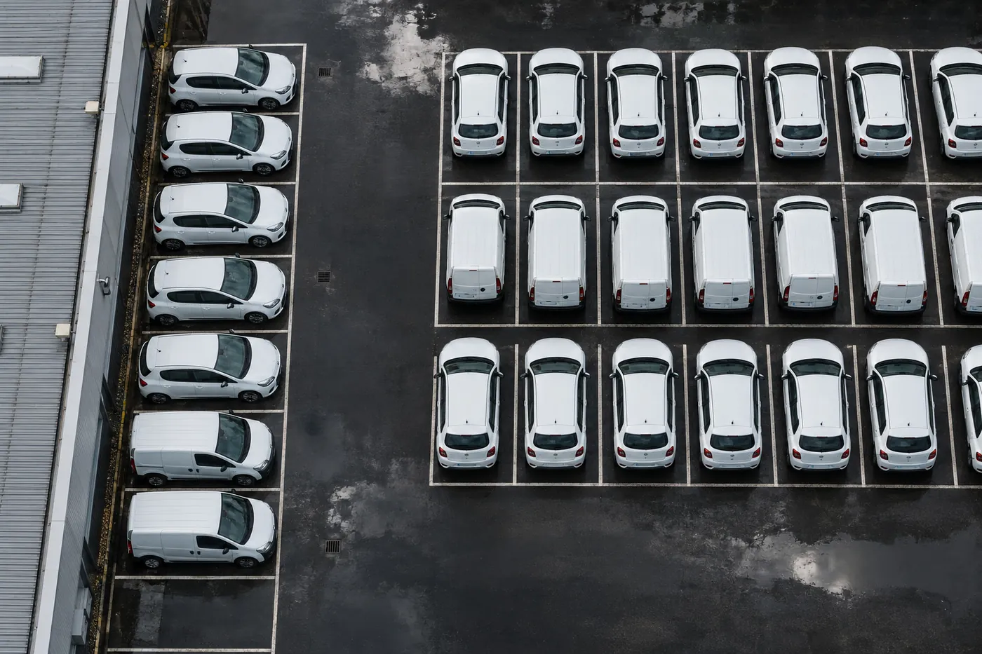 Aerial view of a depot yard with rows of white cars and vans